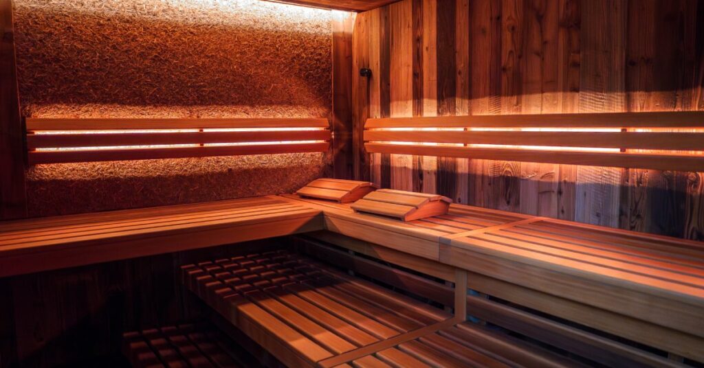 Interior of a sauna with wooden walls and benches on two different levels, with artificial lighting in the ceiling and walls.