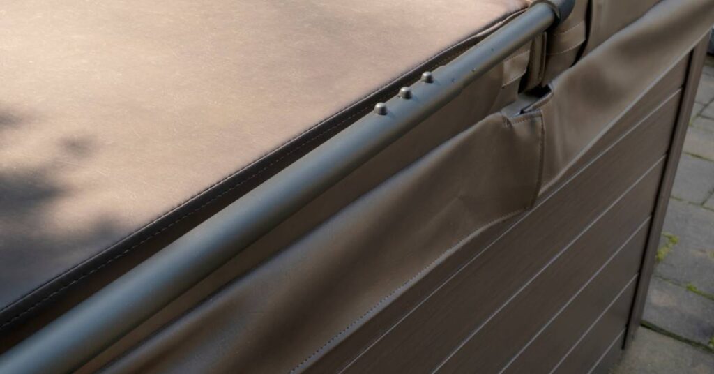 Close-up of a large brown plastic cover with the security bar of a large hot tub placed outdoors over concrete.